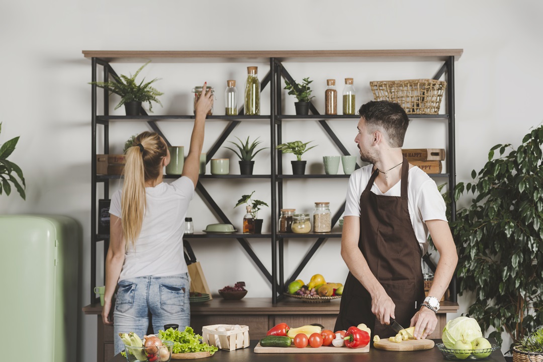 man-cutting-vegetables-looking-woman-taking-bottle-from-shelf